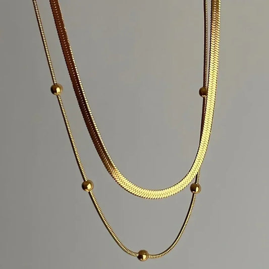 Two gold necklaces on a gray background