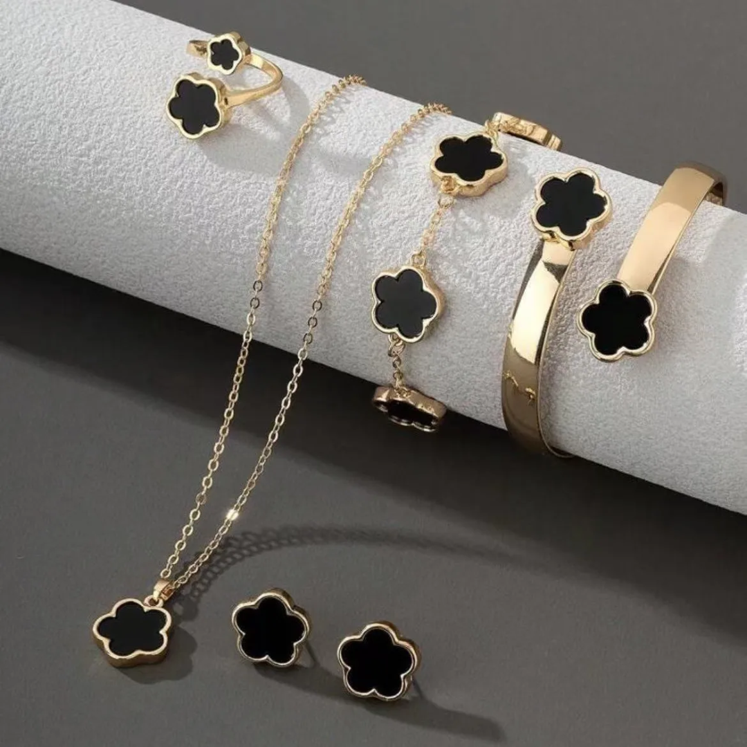 Gold jewelry set with black clover-shaped charms on a gray surface