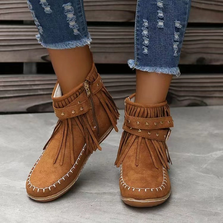 Brown fringe boots worn with ripped jeans on a concrete floor.