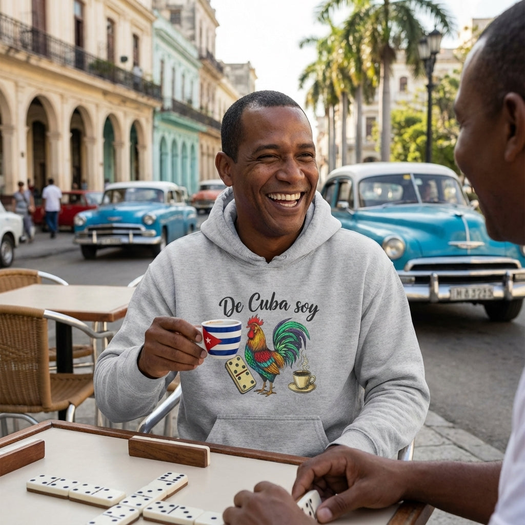 Man in a gray hoodie with a Cuban-themed design, drinking from a mug, playing dominoes on a street in Cuba.