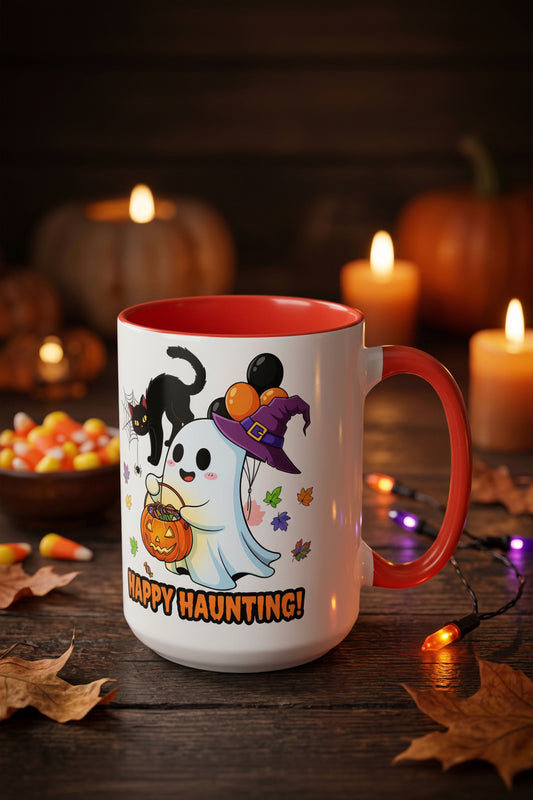 A white ceramic mug with a red handle and interior, decorated with a cute Halloween graphic of a ghost in a witch hat, a black cat, and the words 'HAPPY HAUNTING!'. The mug is set on a rustic wooden table surrounded by autumn leaves, candy corn, and glowing candles in the background.