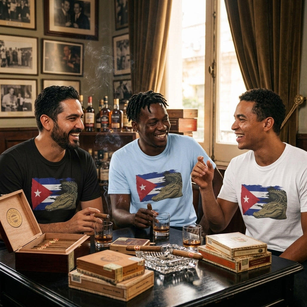Three men laughing together in a warmly lit room, each wearing a graphic t-shirt featuring a Cuban flag and alligator design. The table in front of them is styled with cigars, cigar boxes, and glasses of whiskey.