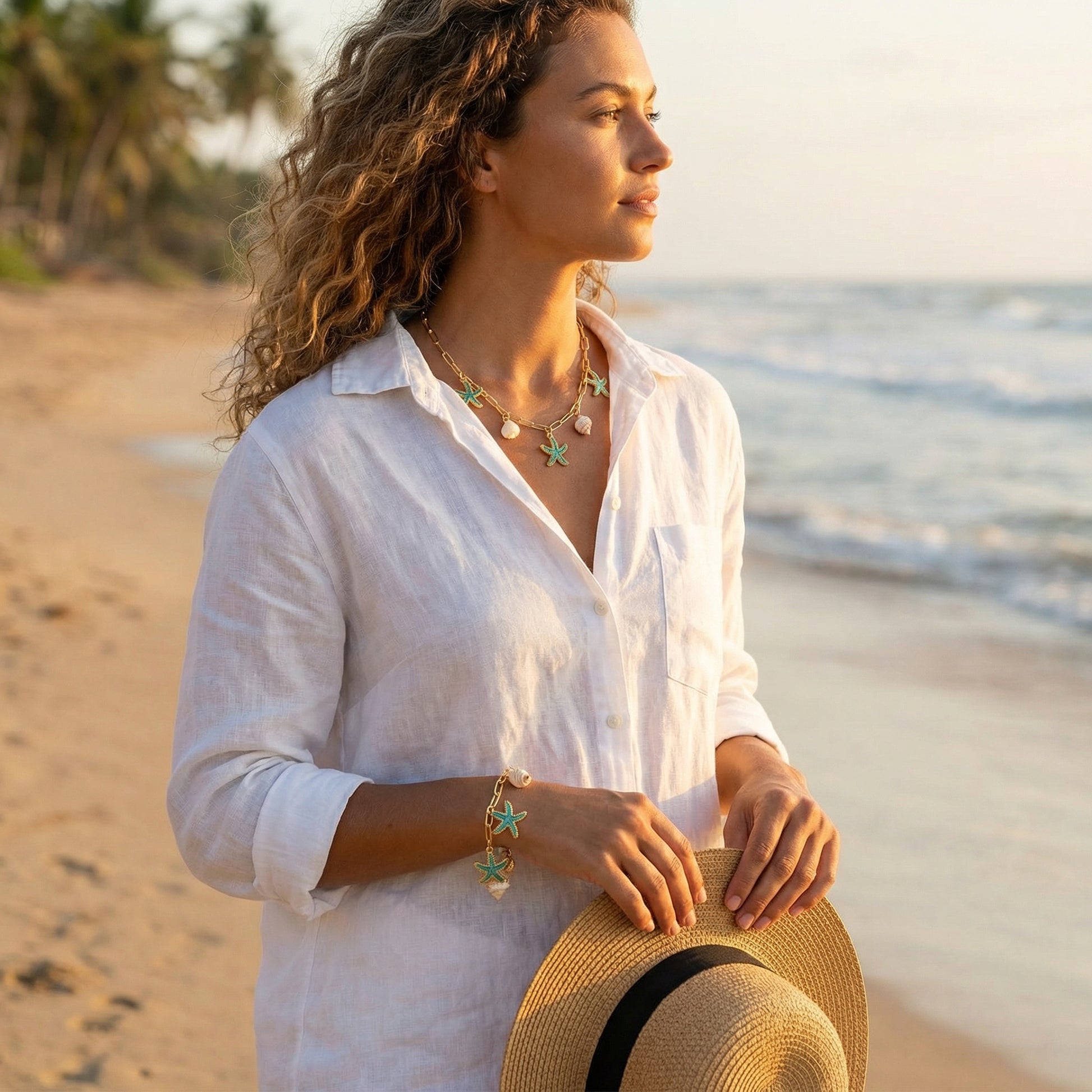 Woman in a white shirt holding a straw hat on a beach at sunset