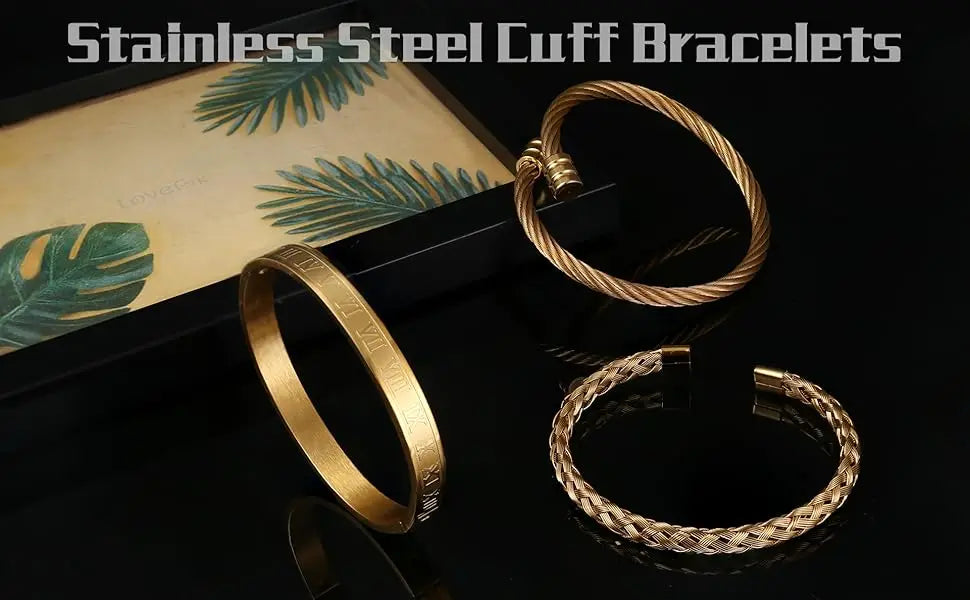 Two gold stainless steel cuff bracelets on a dark surface with green leaf patterns.