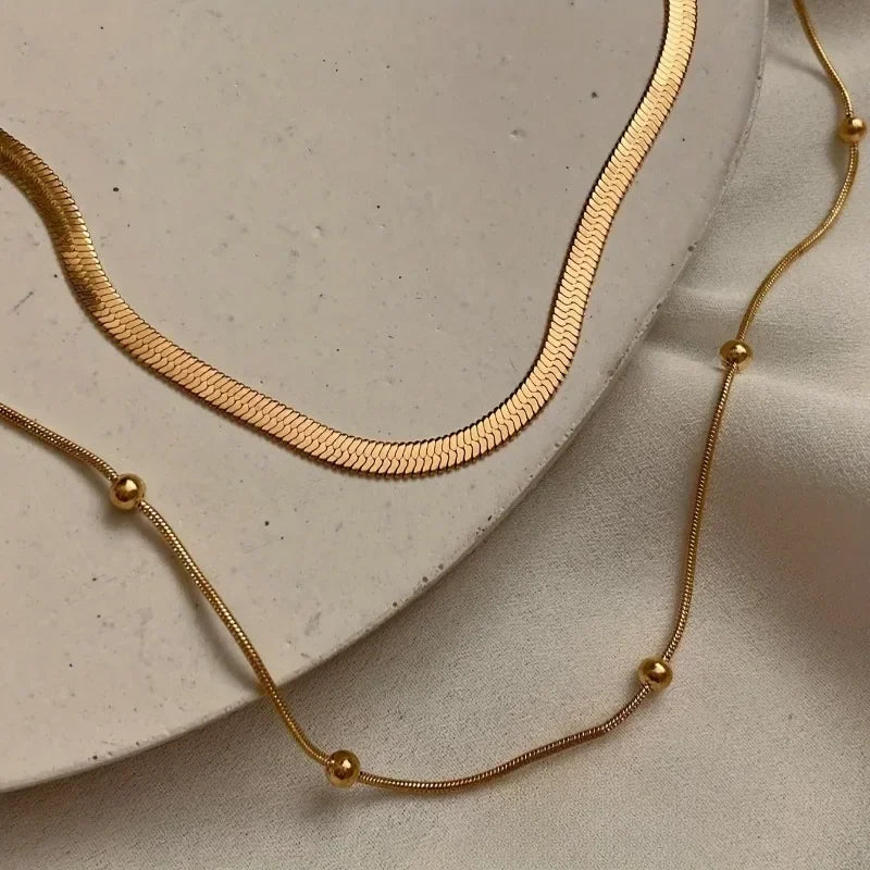 Two gold necklaces on a light beige surface