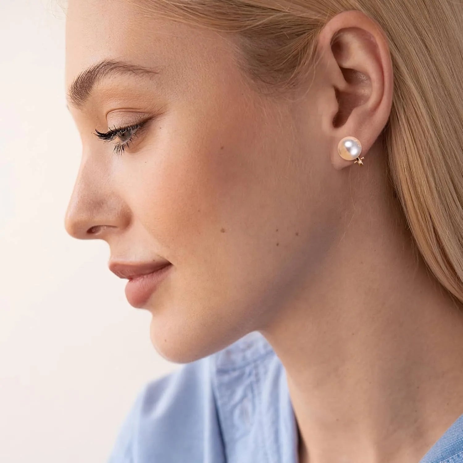 Close-up of a woman wearing pearl earrings with a light background