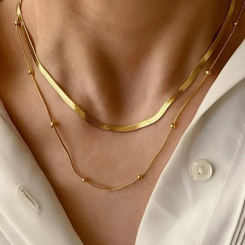 Gold necklaces on a person wearing a white shirt with a visible brand label.