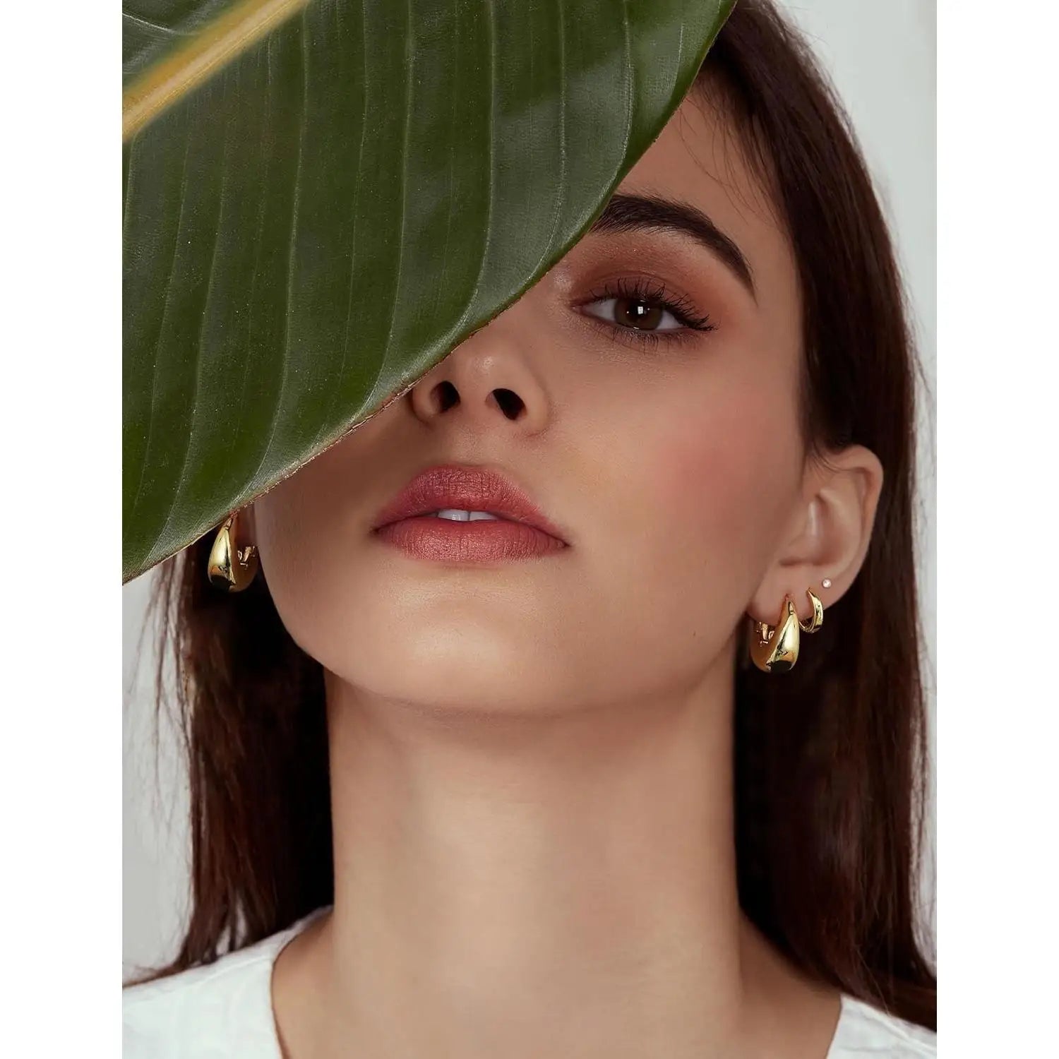 Woman wearing gold earrings with a leaf covering her face