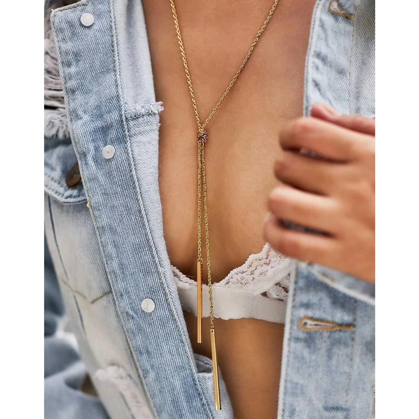 Person wearing a gold necklace with a denim jacket and white lace top.
