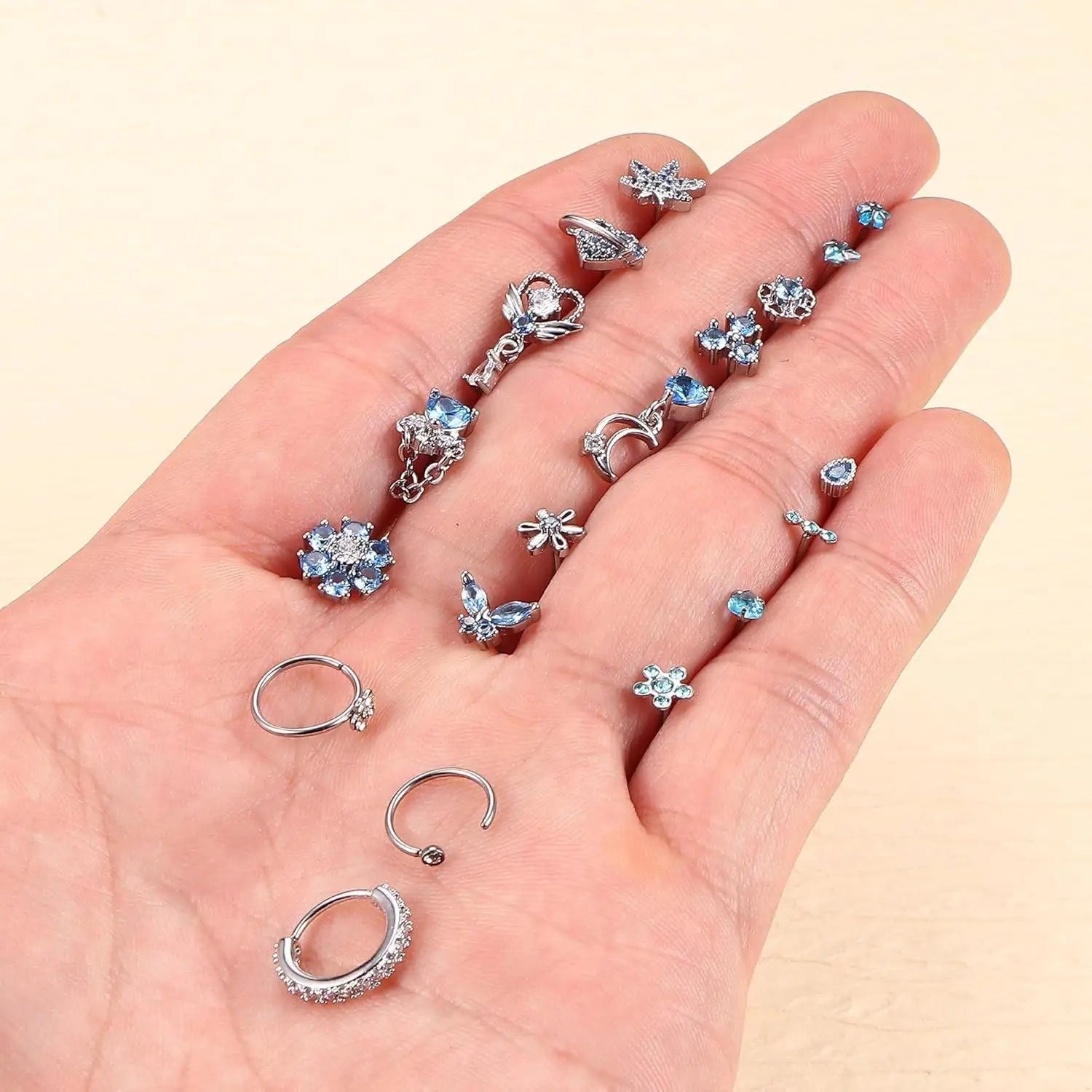 Hand holding various pairs of earrings on a beige background