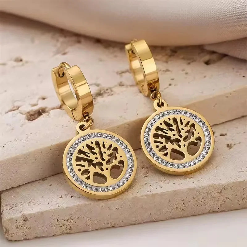 Gold hoop earrings with tree of life design on a beige stone surface