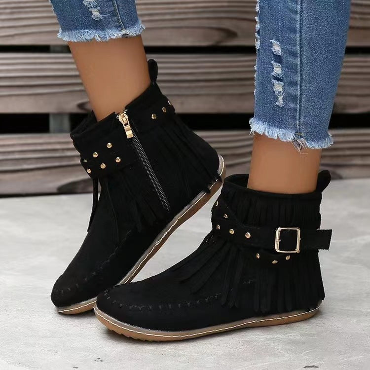 Black fringe boots with gold accents worn with ripped jeans on a neutral background