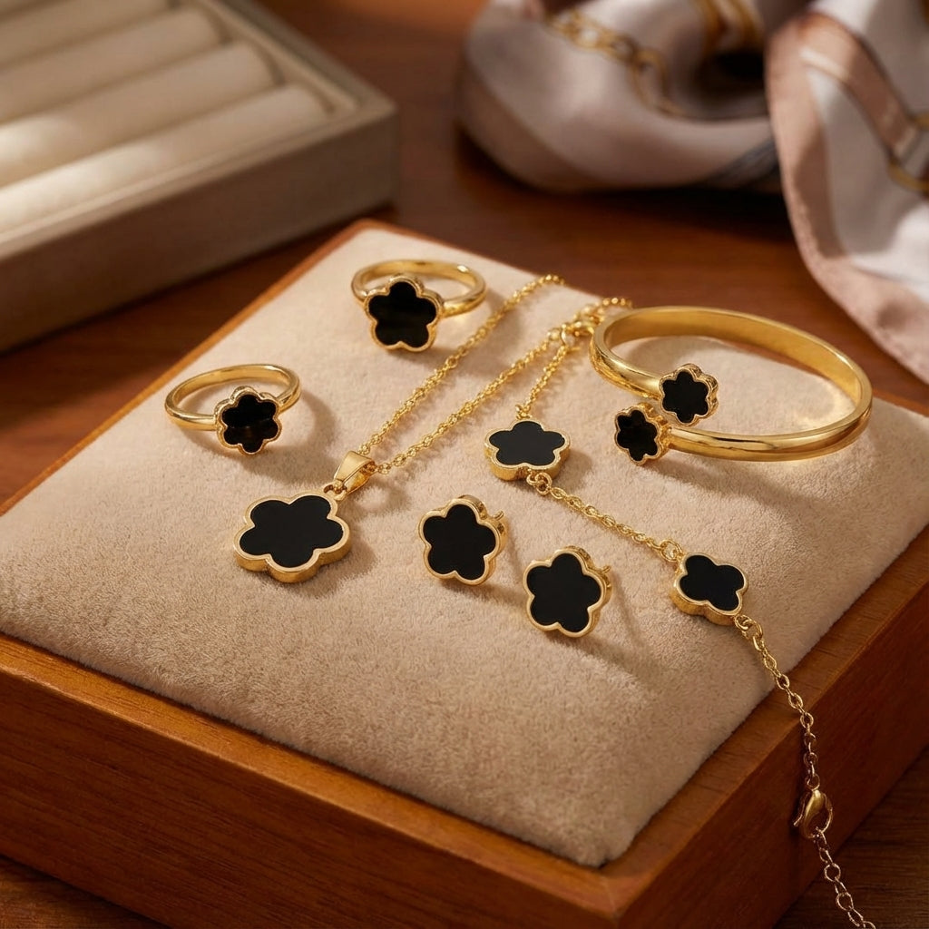 Gold jewelry set with black flower designs on a wooden stand.