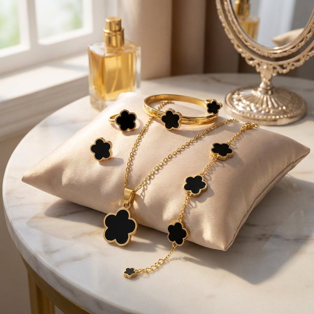 Gold jewelry set with black flower designs on a marble surface.