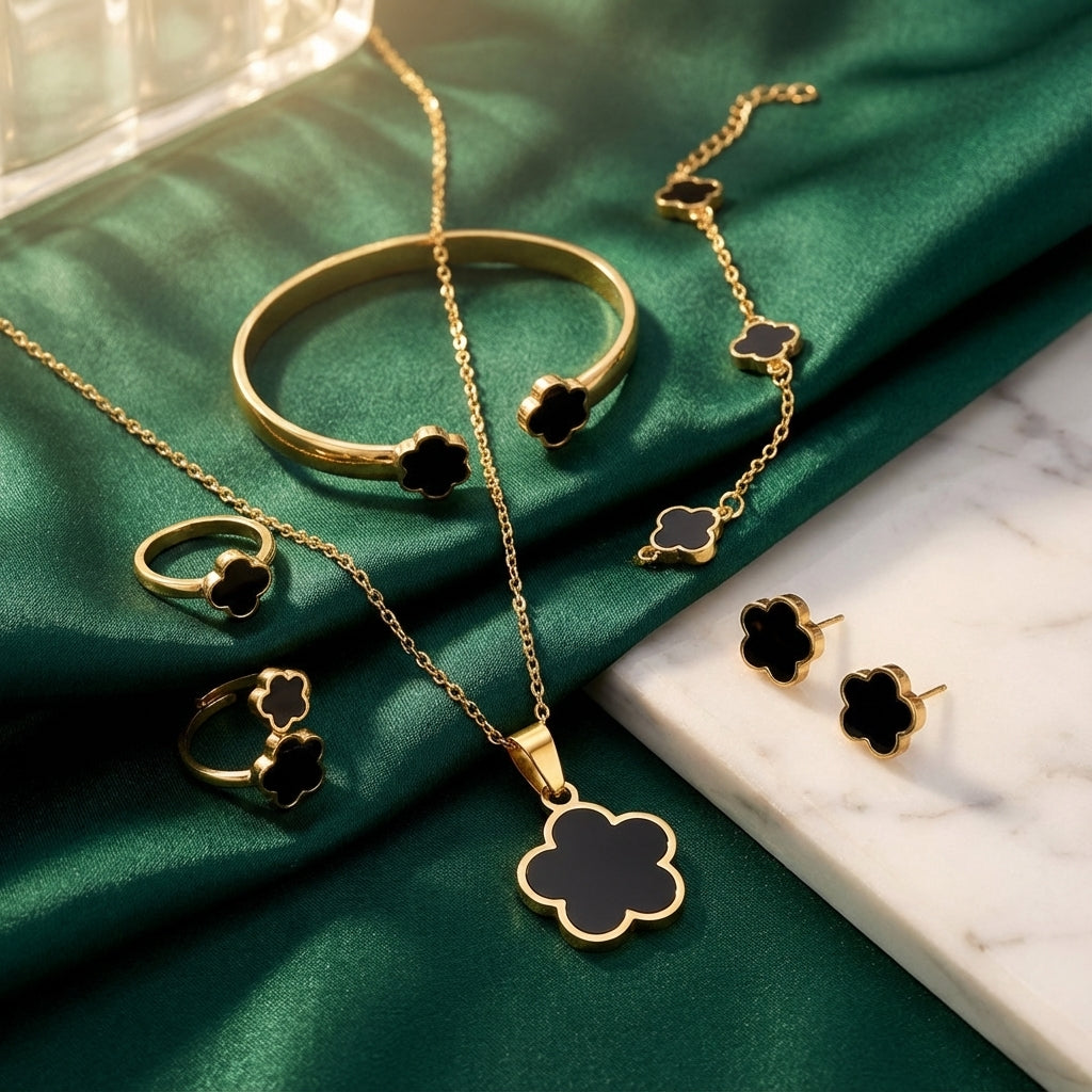 Gold jewelry set with black clover accents on a green fabric background