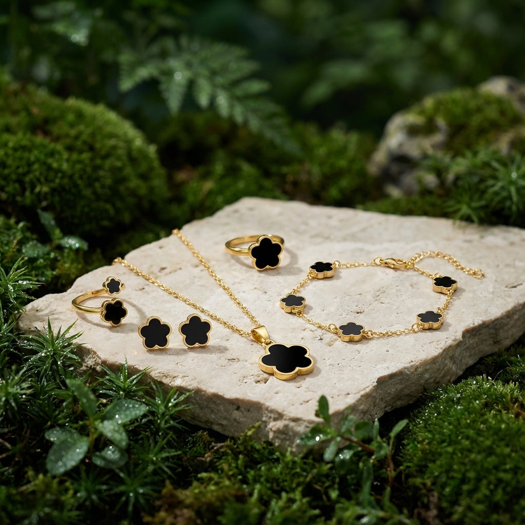 Gold jewelry set with black accents on a stone surface surrounded by greenery