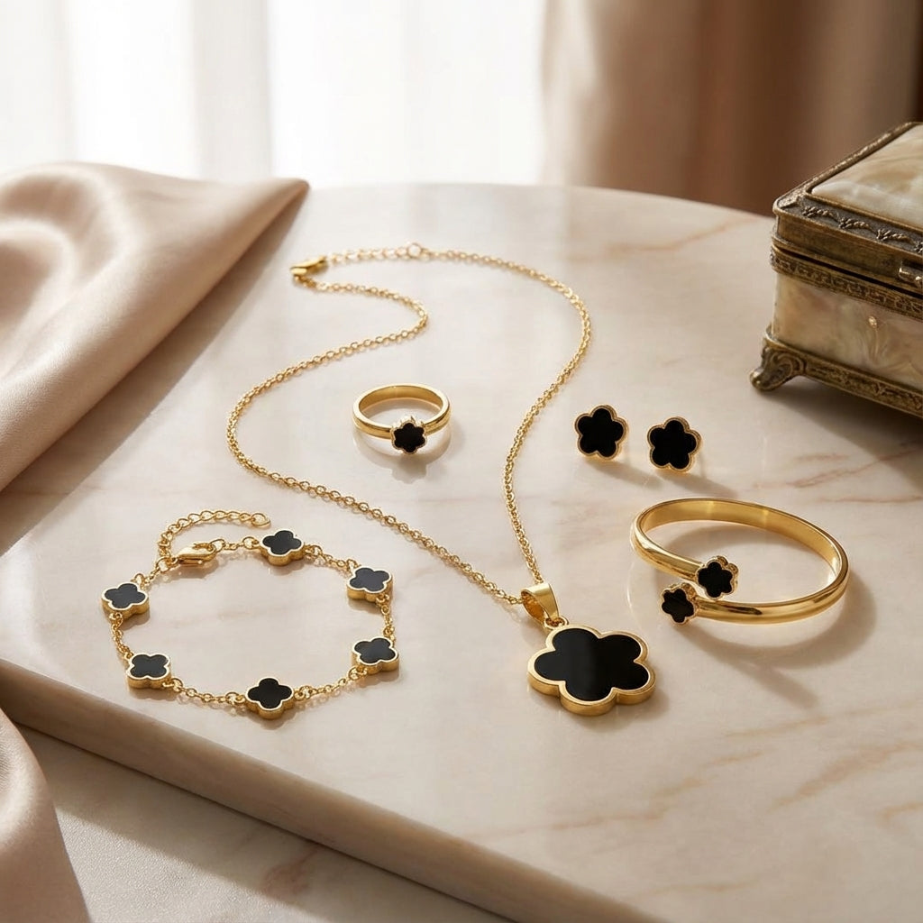 Gold jewelry set with black clover accents on a marble surface